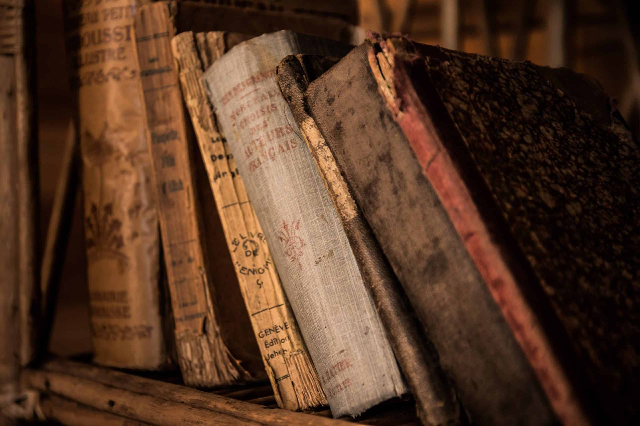 Alte Bücher, die leicht aneinander gelehnt in einem Regal nebeneinander stehen. Sie neigen alle leicht nach links.